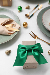Beautiful table setting with Christmas balls and gift on white background, closeup