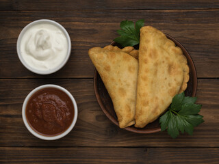 Bowls with red and white sauce and fried pasties on a wooden table.