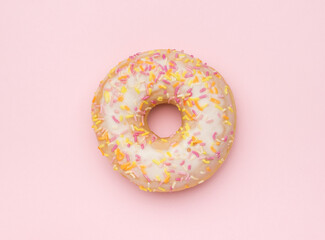 Fototapeta na wymiar A light glazed donut sprinkled with sweet decorations on a pink background. The minimal concept of popular baking.