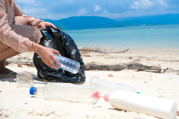 A woman's hands collect plastic waste, water bottles and plastic bottles. and a lot of dirt on the beach She puts it in a garbage bag. concept of environmental protection and global warming reduction