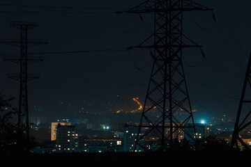 lights of a night city, buildings and houses of a residential area against the background of large high voltage poles, structures of power lines