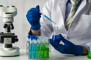 A scientist or a doctor in a lab coat holds a test tube using a reagent microscope and a drop of colored liquid on a glass apparatus doing biochemical laboratory research.