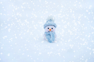 Cute toy snowman in a blue hat and scarf on a snowy background. Christmas and New Year greeting card. Winter concept. Copy space.