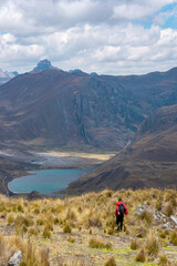 Fototapeta na wymiar Hombre con mochila Caminado en una meseta o páramo, hacia una laguna y una montaña con el cielo nublado, en los Andes Perú Sudamérica 