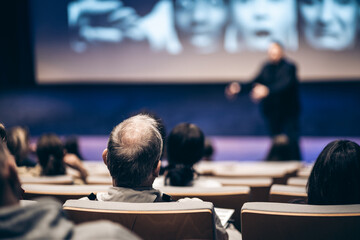 Speaker giving a talk in conference hall at business event. Rear view of unrecognizable people in...