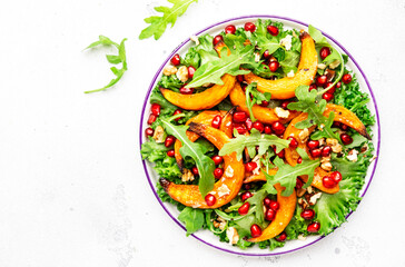 Autumn pumpkin salad with baked honey pumpkin slices, lettuce, arugula, pomegranate seeds and walnuts. Healthy vegan eating, comfort food. Top view