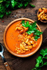 Spicy pumpkin creamy soup with mushrooms, pepper and parsley. Winter or autumn healthy vegan vegetarian food. Soup bowl on rustic wooden table background. Top view