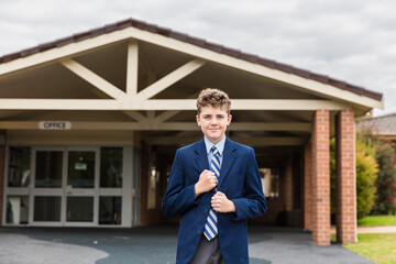 Child in uniform standing in front of school office holding blazer smiling