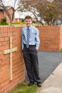Child standing with hands in pockets leaning against brick entrance with cross to private school