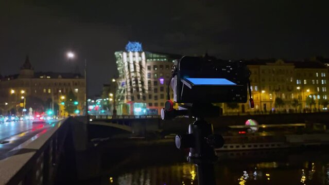 Camera on tripod making night time lapse of Prague traffic, Dancing House blurry lights background
