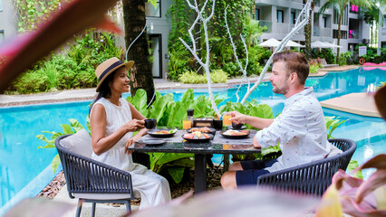 Couple having breakfast by the pool during vacation. Asian Thai women and caucasian men having...