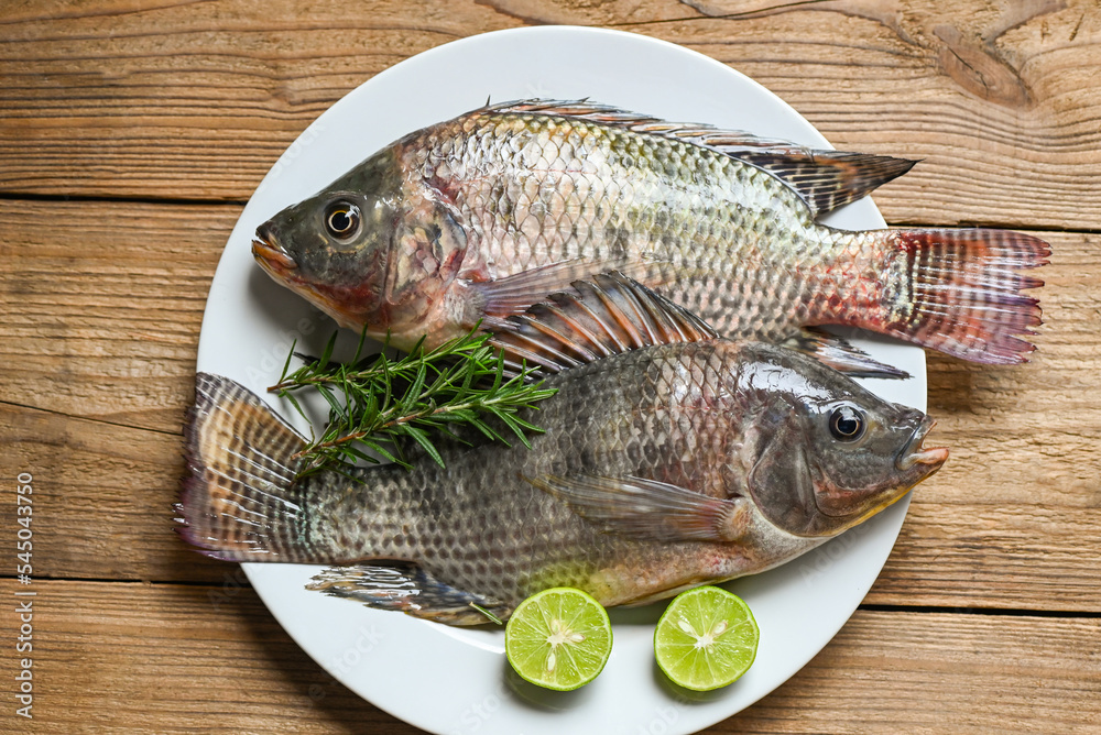 Wall mural fresh raw tilapia fish from the tilapia farm, tilapia with white plate with rosemary lemon lime on w