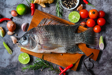 Tilapia with spice rosemary tomato lemon lime ginger garlic pepper chili on dark background, Fresh raw tilapia fish from the tilapia farm