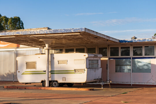 A large retro style caravan parked under the canopy of an abandoned service station