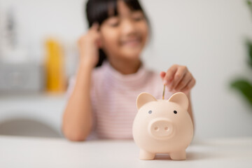 Little Asian girl saving money in a piggy bank, learning about saving, Kid save money for future education. Money, finances, insurance, and people concept