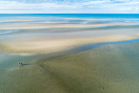 Aerial view of two fishermen walking over tidal sand flats towards deeper water.