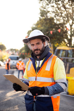 Man road worker with beard wearing white hat with yellow and orange jacket holding his notes