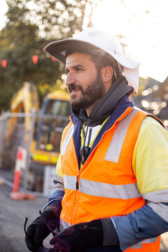 Close up shot of a smiling road worker man with white hat wearing high vis orange jacket workwear