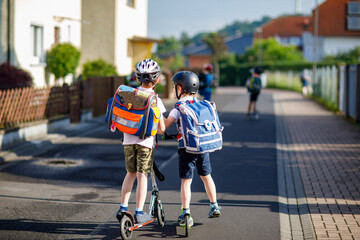 Two school kid boys in safety helmet riding with scooter in the city with backpack on sunny day....