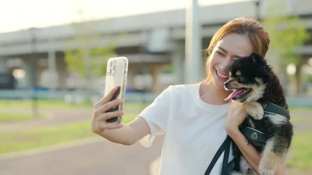 Happy young asian woman walking in public park and photo selfie with her dog. Pet lover concept