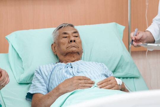 professional doctor standing by explain the treatment information via male elderly patient lying in bed in private hospital sickroom. The treatment program is suitable for people to socialize elderly