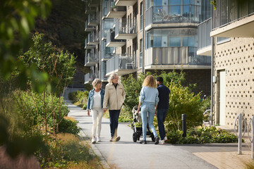 Senior and young couple with baby stroller walking in residential area