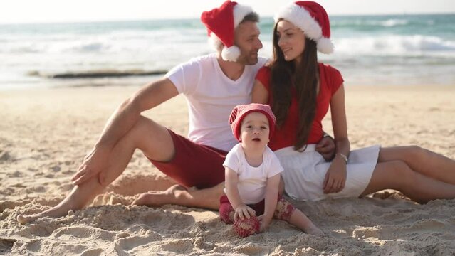 Happy family enjoy on beach in vacation, holiday in new year and Christmas. sit on sand get fun near sea together. white and red clothes and Santa hats.