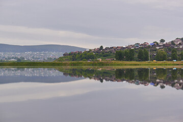 view of a beautiful city by the lake surrounded by low mountains. the city is reflected in the water of the lake