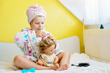 Cute smiling little girl child playing with her doll at home. Preschool child in bathrobe after...