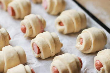 rolled dough blanks for croissants with sausages on a baking sheet before baking selective focus