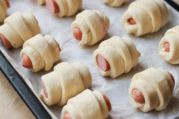 rolled dough blanks for croissants with sausages on a baking sheet before baking selective focus