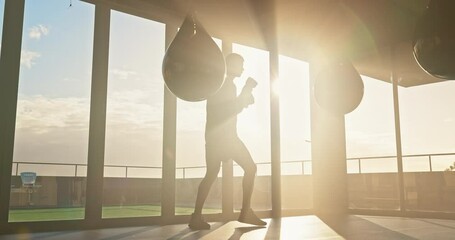 Boxer, fitness and punching bag by man at sunrise for exercise, power and training in fitness studio. Mma, fighter and workout by sports guy intense punching, energy and endurance practice at sunset