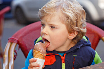 Cute adorable kid boy eating ice cream in outdoor cafe. Happy child on sunny day. Healthy toddler...