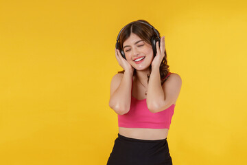 Naklejka premium Portrait of Happy young woman listening music in headphones and singing while standing isolated over yellow background