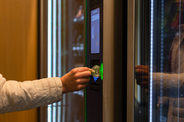 Woman's hand putting a bitcoin coin in a vending machine. Concept of sale, technology and consumption