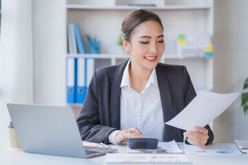 Portrait of beautiful smiling young entrepreneur businesswoman holding cup of coffee and working on laptop computer at office. Panoramic background.