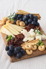 Cheese plate served with grapes, olives, crackers and dried tomatoes on a wooden background,...