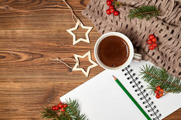 Christmas composition of open blank notepad, coffee cup, scarf and fir branches on wooden background