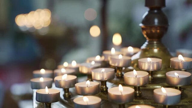 Yellow candle in front with many out of focus candles in background of church