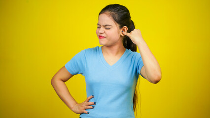 Young woman putting a finger into her ear, isolated over yellow background