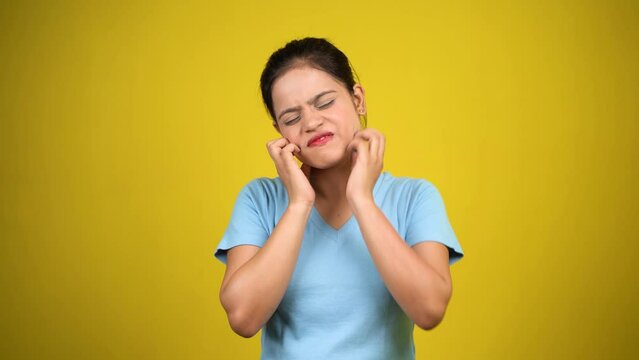 Young woman scratching face or cheek, isolated over yellow background. Annoying itching and rashes due to allergic reaction