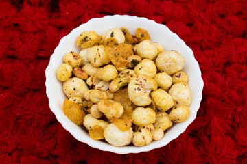 Crispy, healthy and homamade Phool Makhana or Fox Nuts snack. It contain Makhana mixture having peanut and cornflakes. red background.