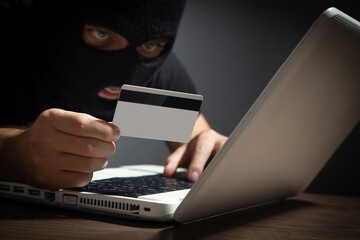 Hacker with credit card and laptop computer. Cyber crime