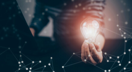 Businessman hand holding light bulb with icons and working on the desk, Creativity and innovation are keys to success.Concept of new idea and innovation with energy and power , working at home,