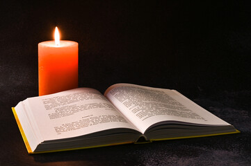 Open book and burning candle on dark background 