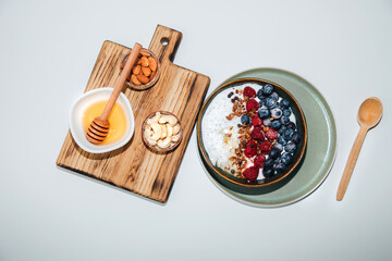 Yoghurts in green plate with blueberries, raspberries, chia seeds and granola with a wooden board on a white background. The concept of healthy eating. Flat lay
