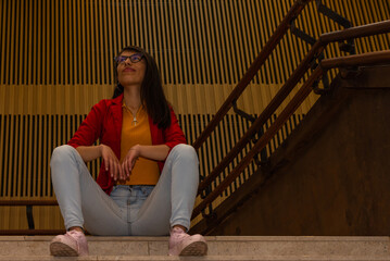Casual dressed Hispanic young woman sitting on a stair step in an industrial interior