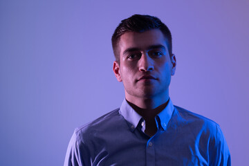 A man in a shirt poses on a dark multicolored neon background