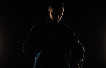 Portrait of a guy putting on his shirt and posing in studio while standing, silhouette