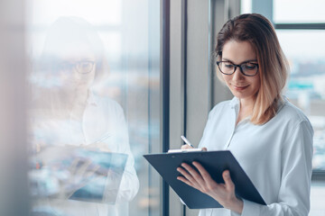 Fototapeta premium Young woman holding a folder of documents and a pen in a modern office.